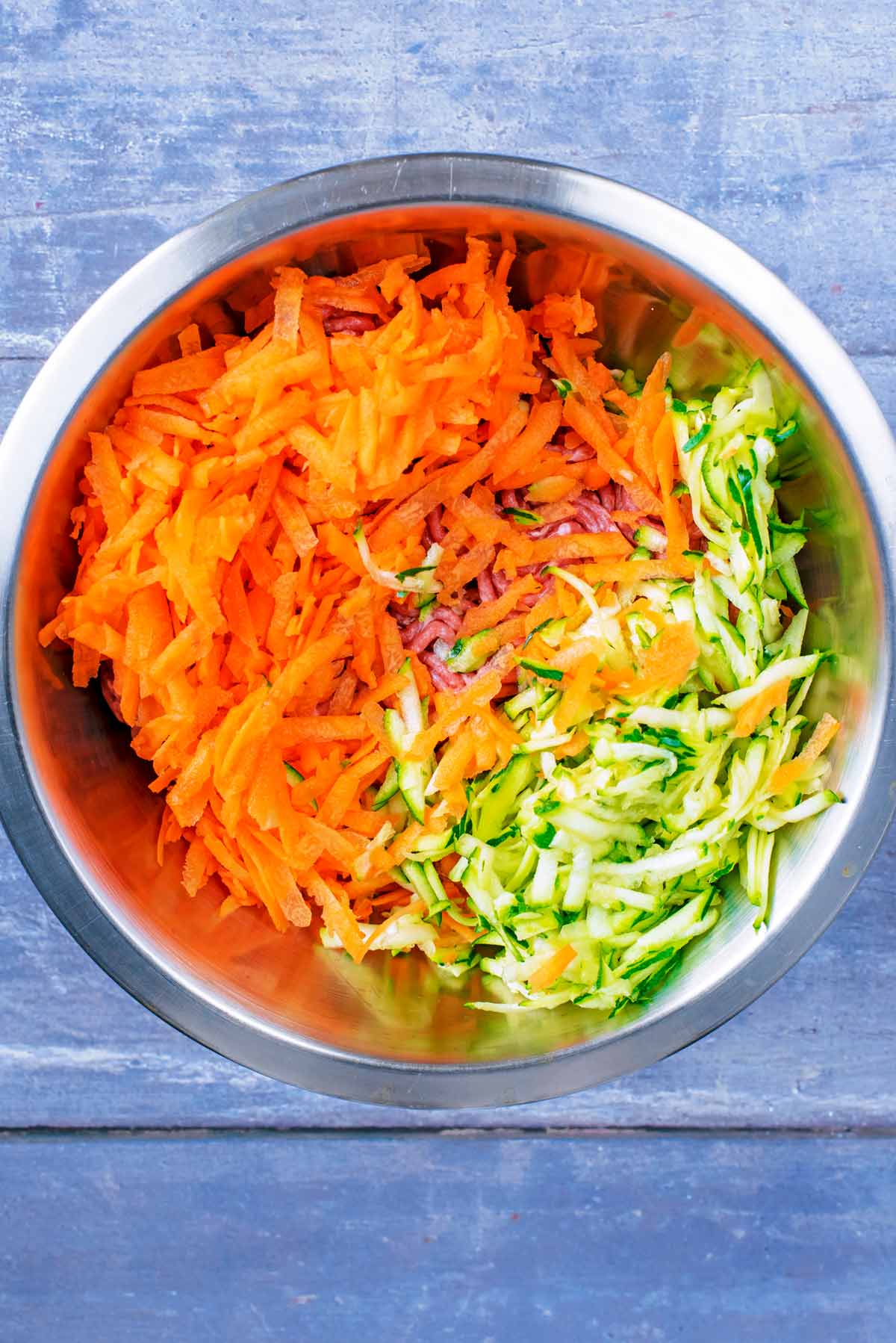 a mixing bowl containing shredded vegetables and beef mince.