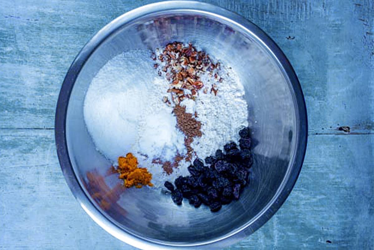 Flour, sweetener, raisins, spices and orange zest in a metal mixing bowl