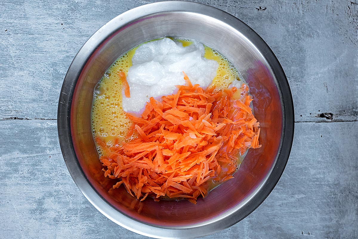 Grted carrot, whisked eggs and yogurt in a metal mixing bowl