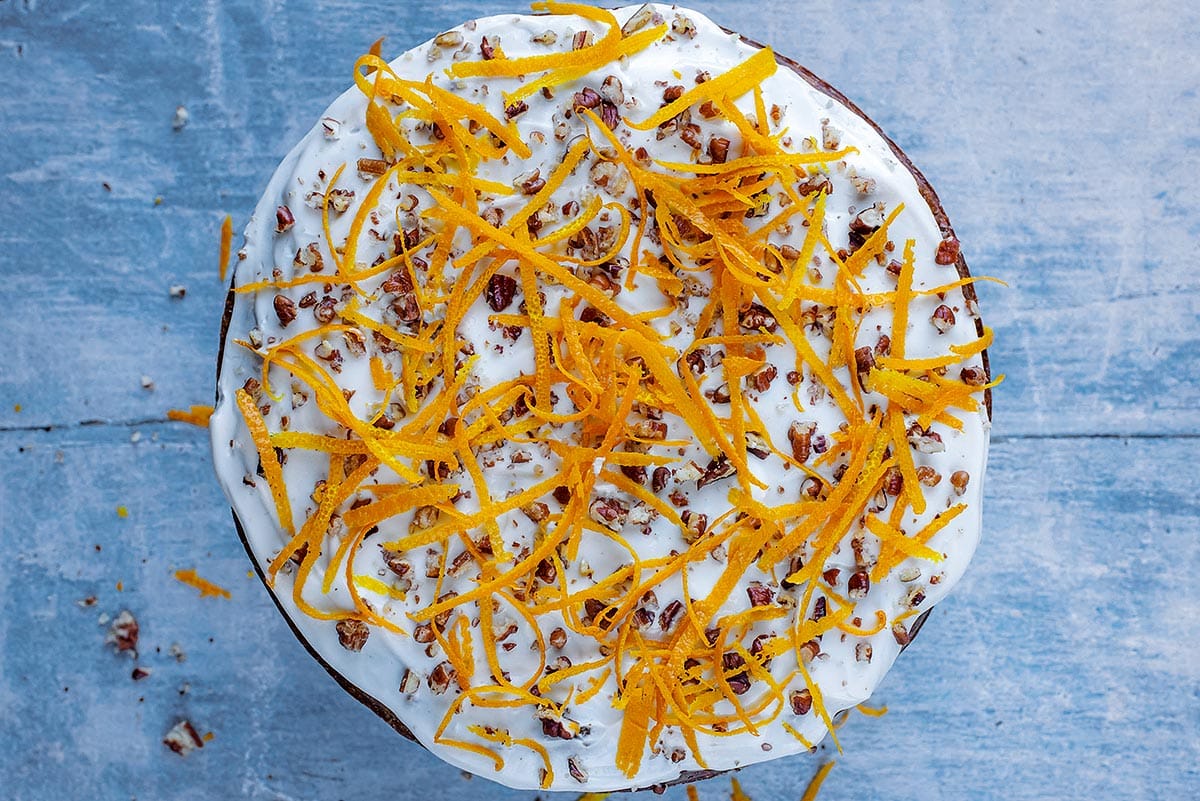 A carrot cake topped with icing, orange rind and chopped pecans