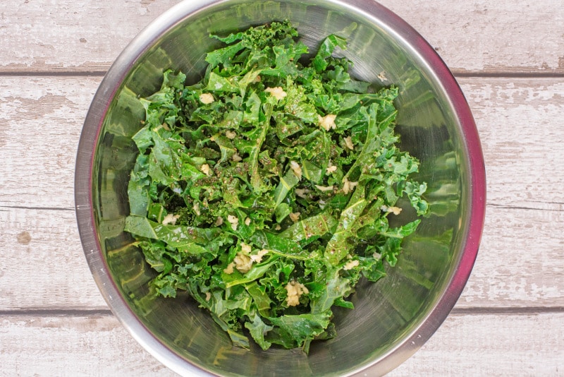 A metal bowl containing chopped raw kale covered in a dressing.