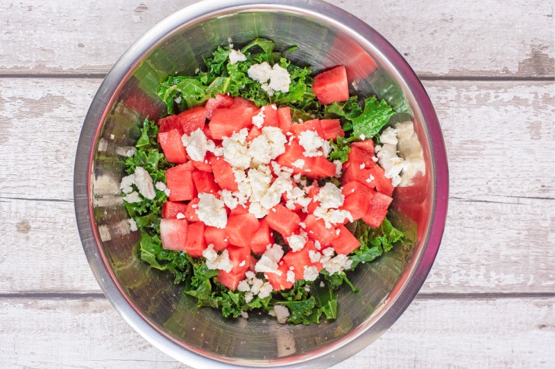 A metal bowl containing chopped raw kale, chopped watermelon and crumbled feta.