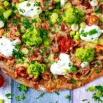 A pizza topped with tomatoes, guacamole and sour cream.