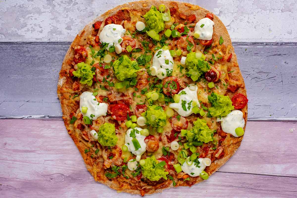 Pizza topped with sour cream, guacamole, and spring onions.