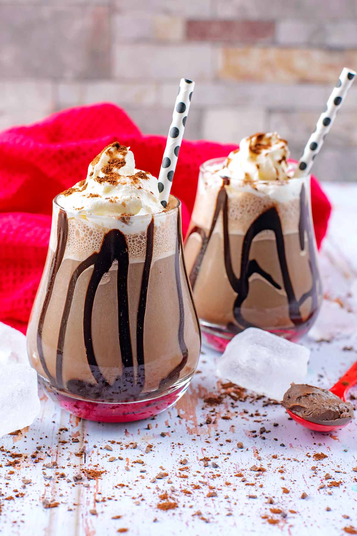 Two glasses of frappuccino topped with cream and chocolate sauce.