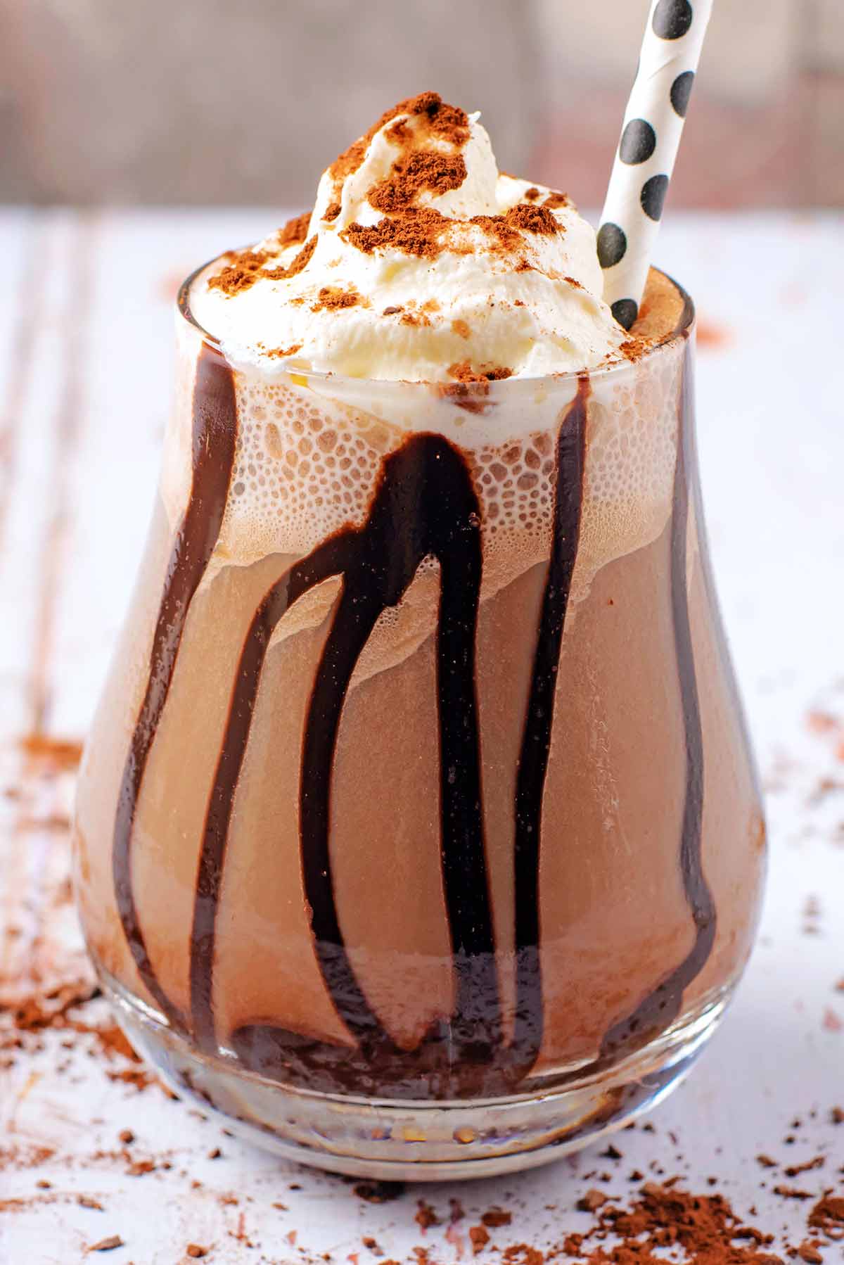 A tall glass of mocha topped with cream and cocoa powder.