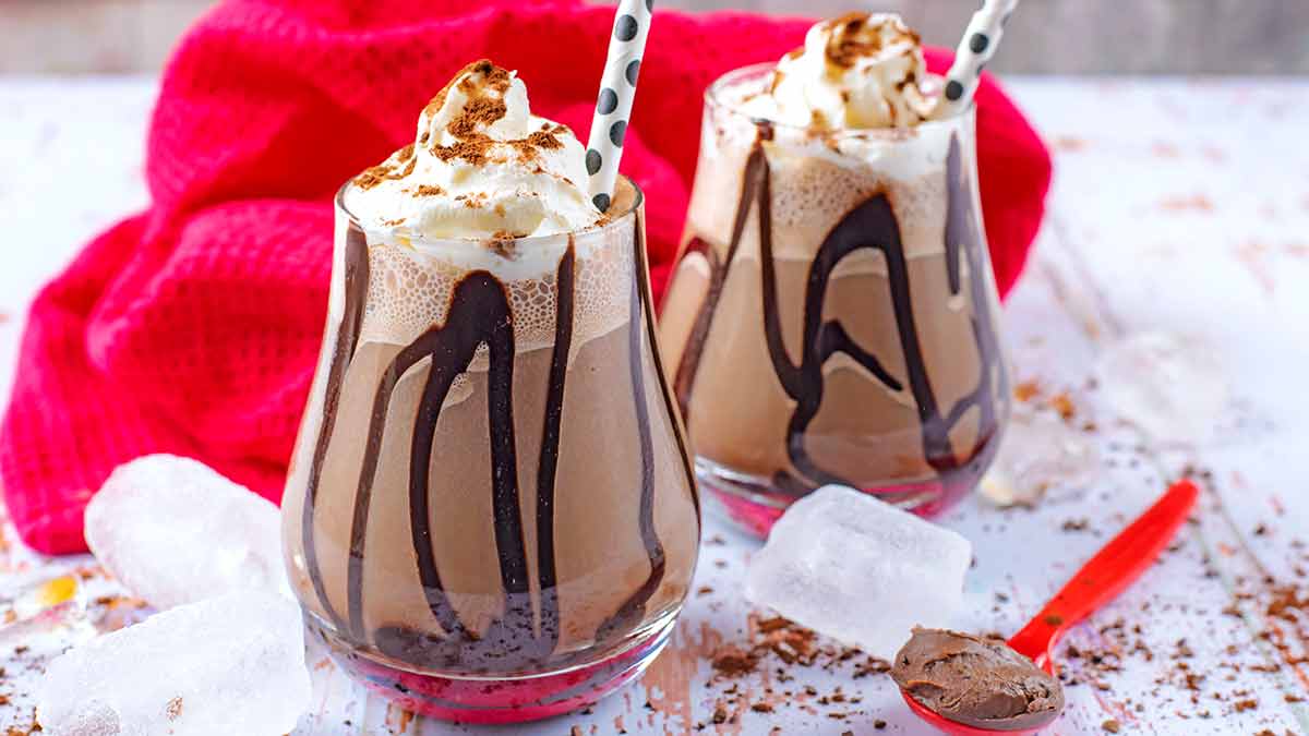 Two glasses of frappuccino with chocolate sauce drizzled in the glass.