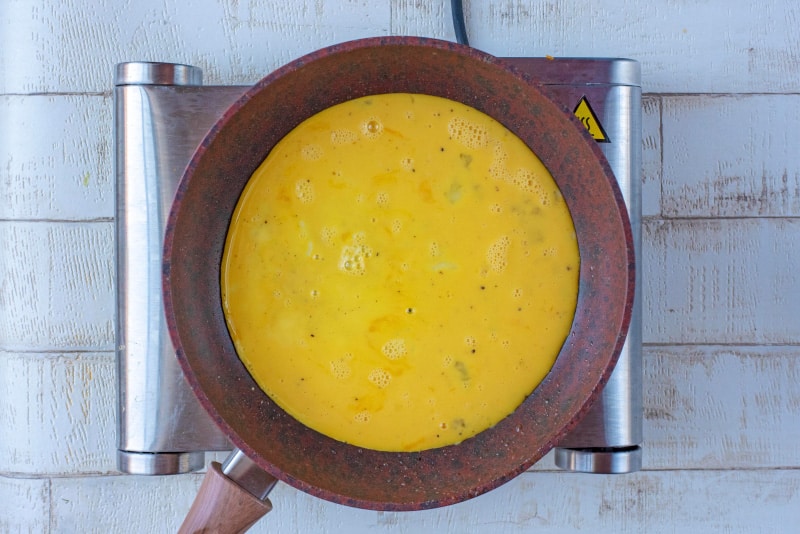 A frying pan containing whisked eggs.