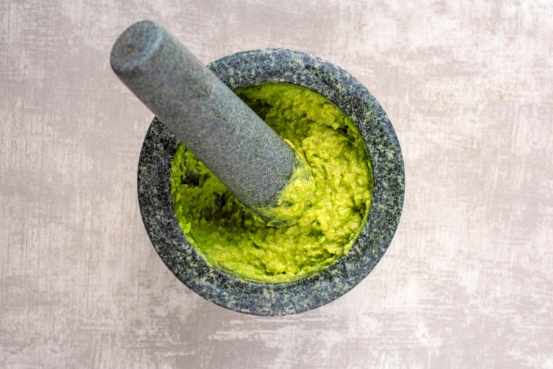 A pestle and mortar with smashed avocado.