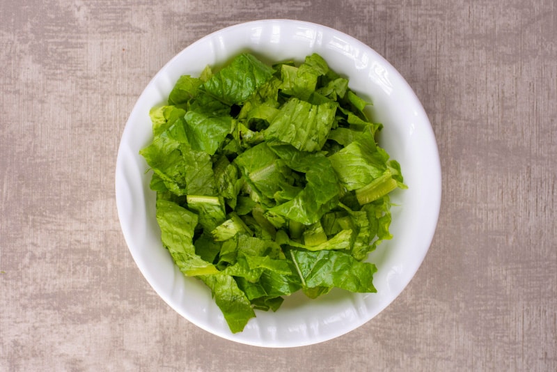 A white bowl containing shredded lettuce.
