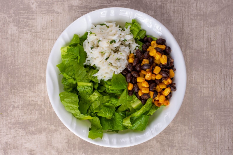 A white bowl containing shredded lettuce, rice, sweetcorn and black beans.