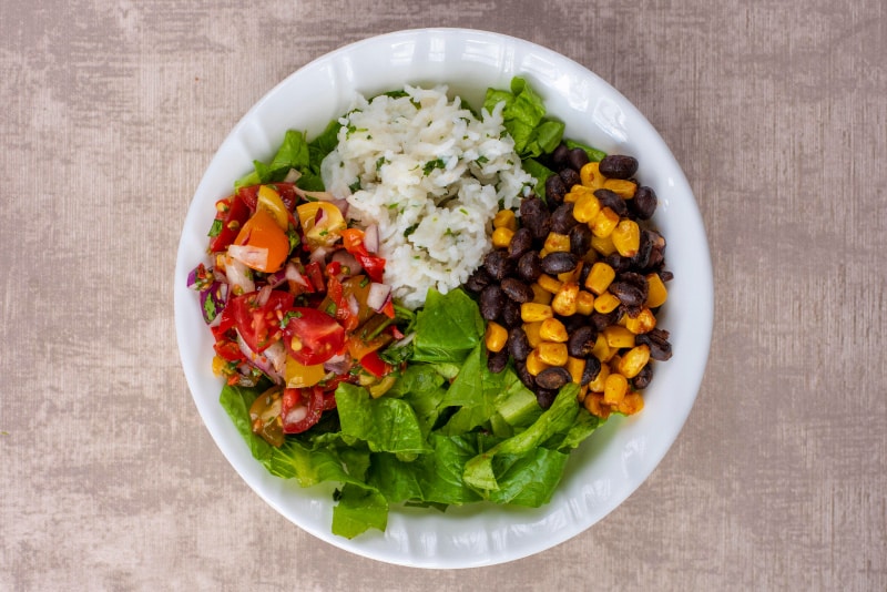 A white bowl containing shredded lettuce, rice, sweetcorn, black beans and salsa.