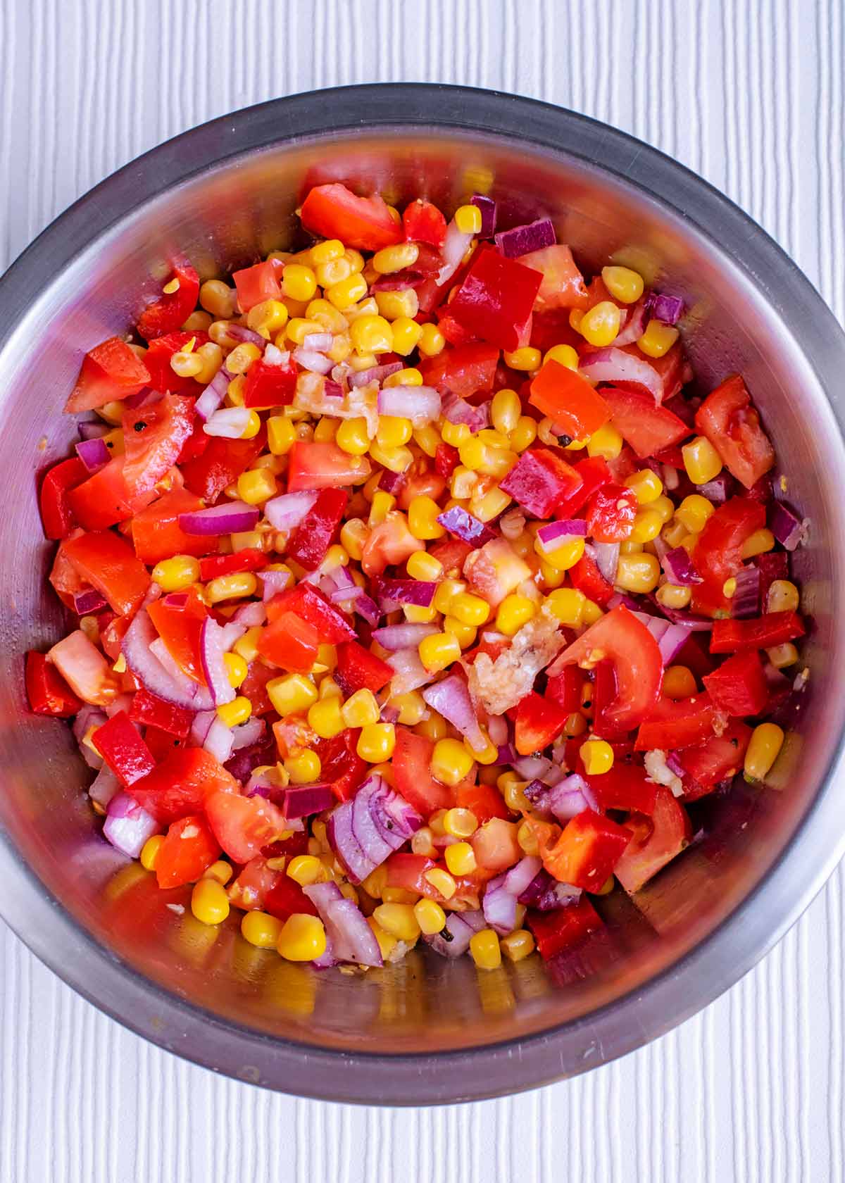 A metal bowl containing sweetcorn, red pepper, tomatoes and red onion.