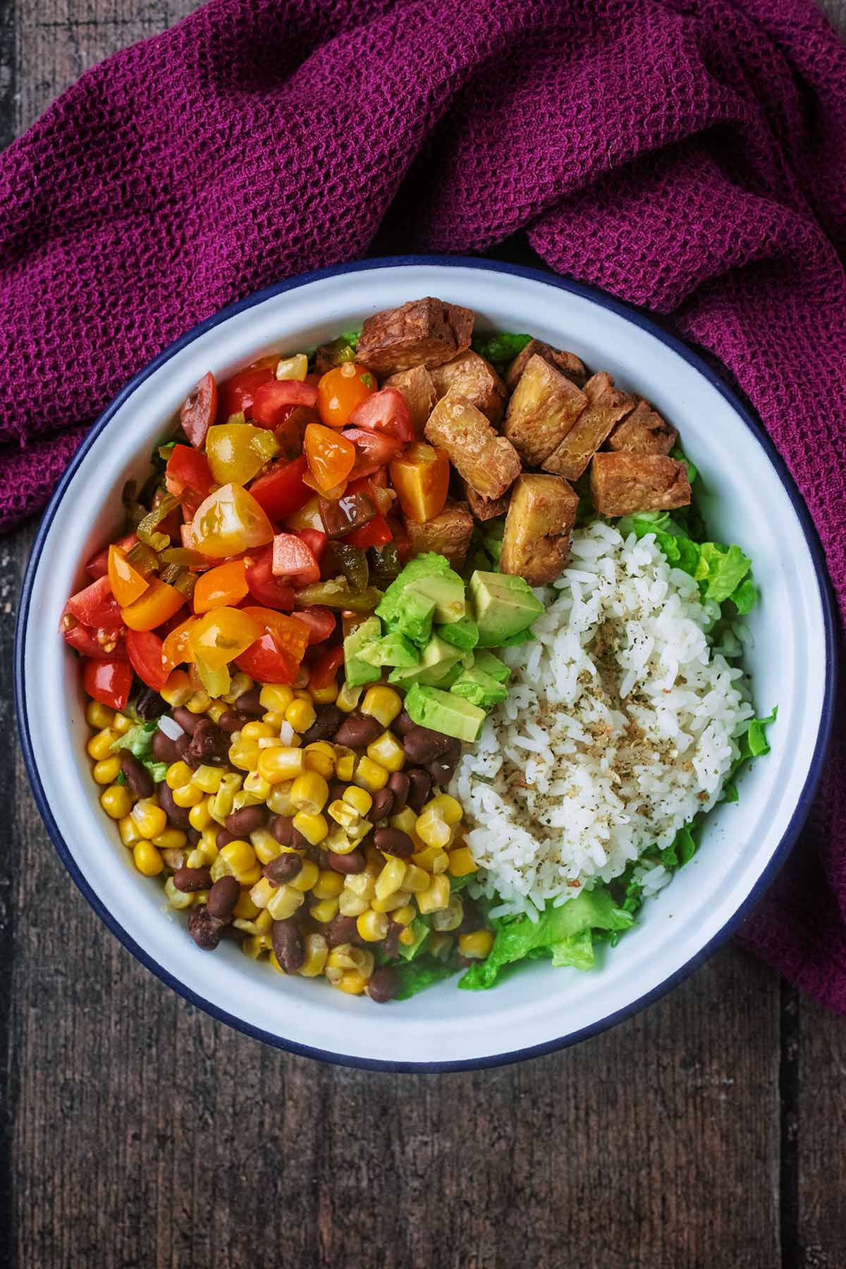 A burrito bowl made up of lettuce corn, beans, salsa and tofu.
