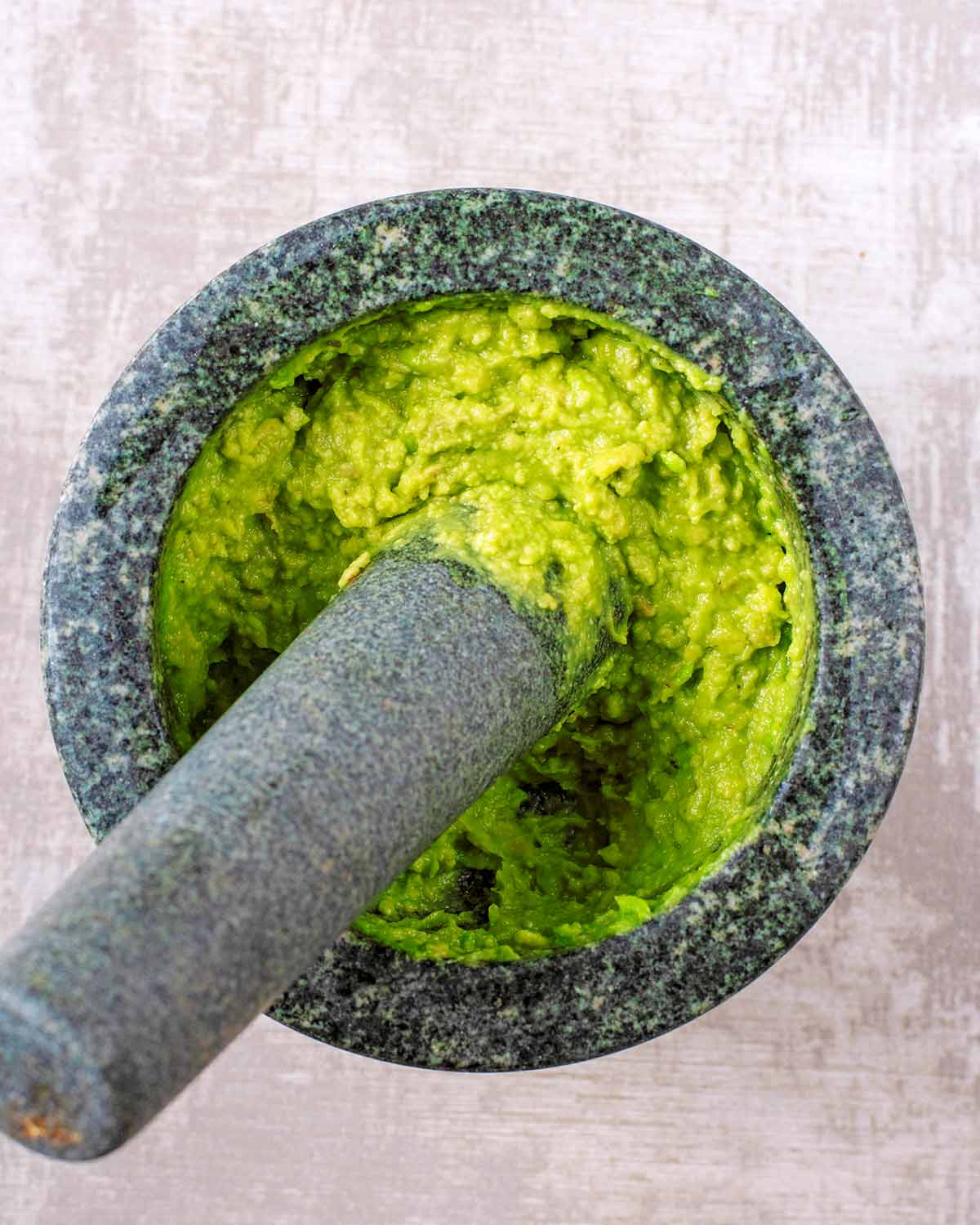A pestle and mortar with smashed avocado.