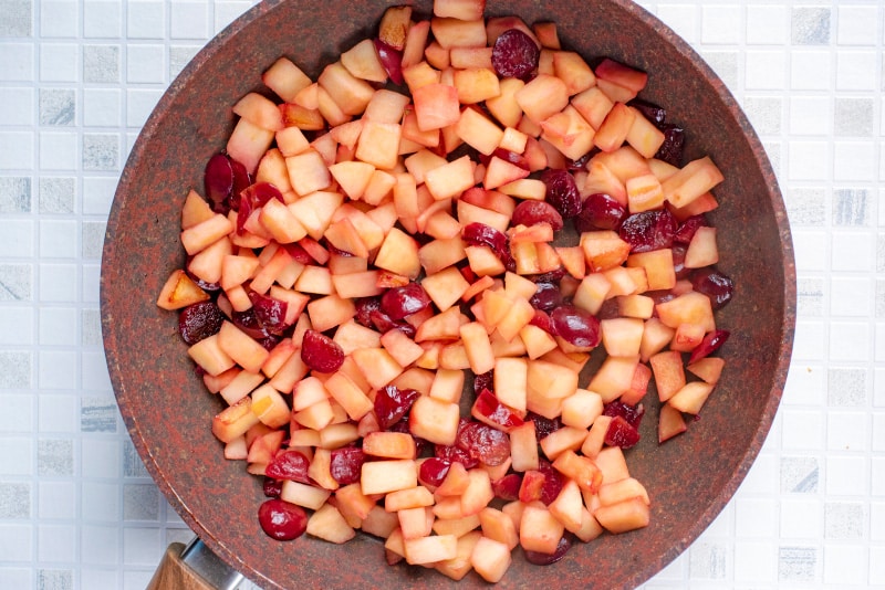Chopped apples and cherries in a frying pan.