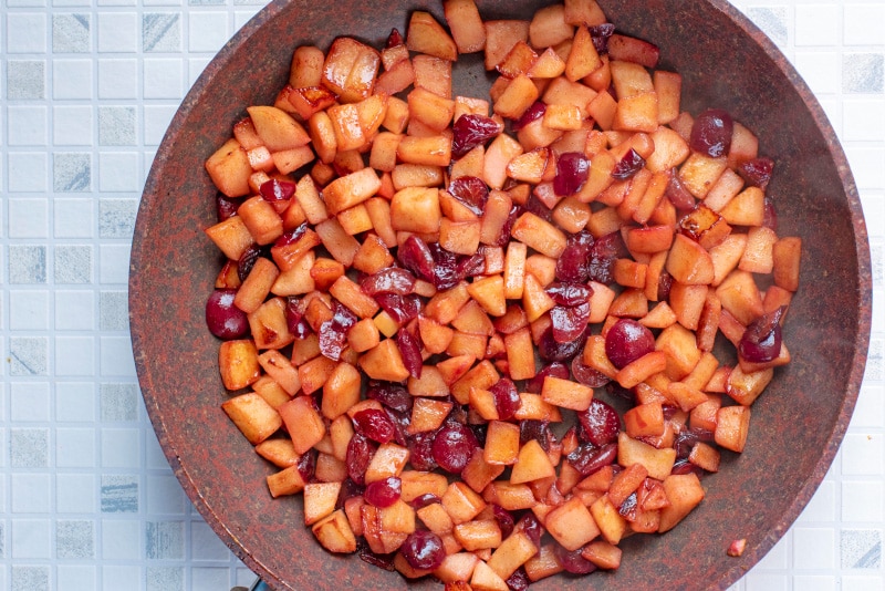 Cooked chopped apples and cherries in a frying pan.