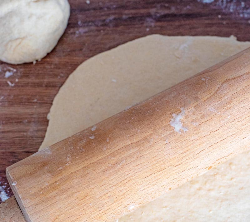 A ball of dough next to rolled out dough and a rolling pin.