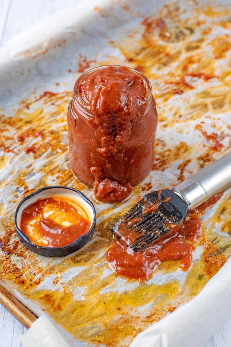 A jar of bbq sauce on a baking tray with a marinade brush.