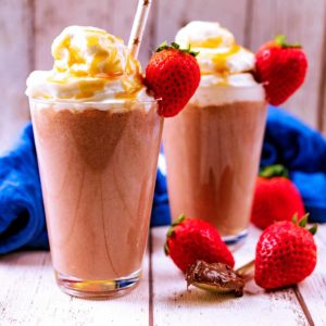 Two glasses of Nutella Smoothie topped with whipped cream and strawberries.