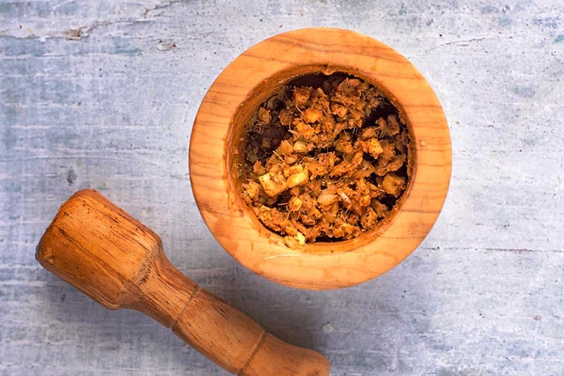 A wooden pestle and mortar containing a brown curry paste.