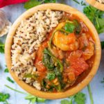 Prawn, Tomato and Coconut Curry and rice in a wooden bowl. Coriander leaf is scattered around it.