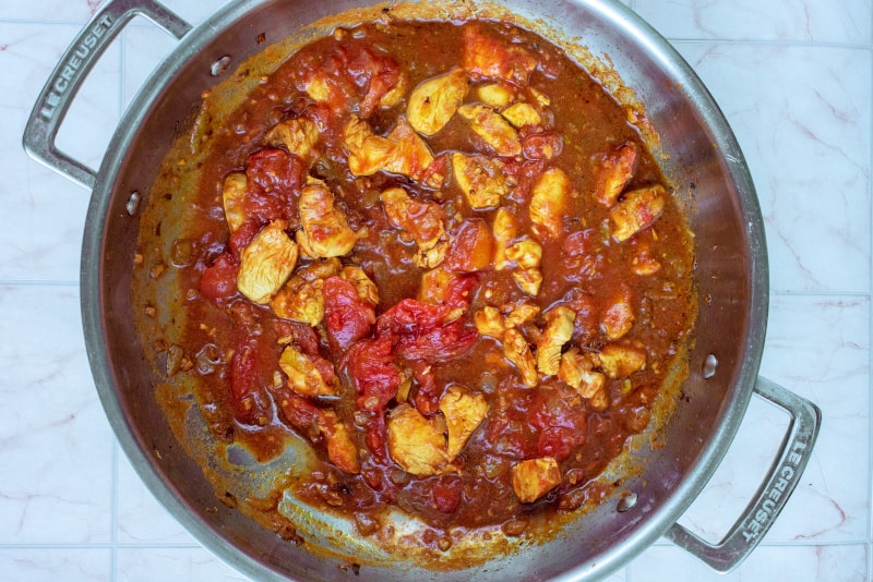 Diced chicken, chopped onions and garlic in a tomato sauce cooking in a large silver pan.