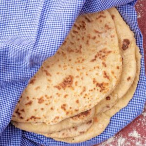 Easy Homemade Flatbreads wrapped in a towel. Flour is sprinkled around.