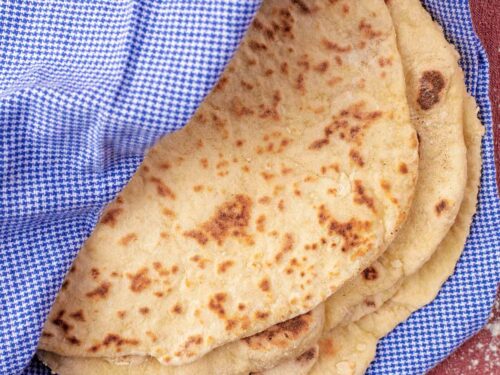 Easy Homemade Flatbreads wrapped in a towel. Flour is sprinkled around.