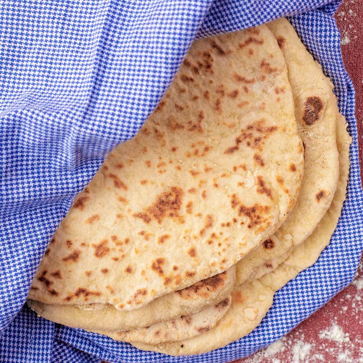 Easy Homemade Flatbreads wrapped in a towel. Flour is sprinkled around.