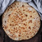 A stack of homemade flatbreads on a wooden surface.