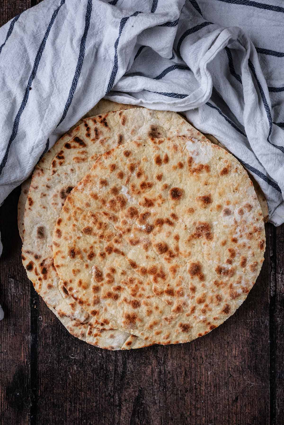 Flatbreads on a wooden surface next to a striped towel.