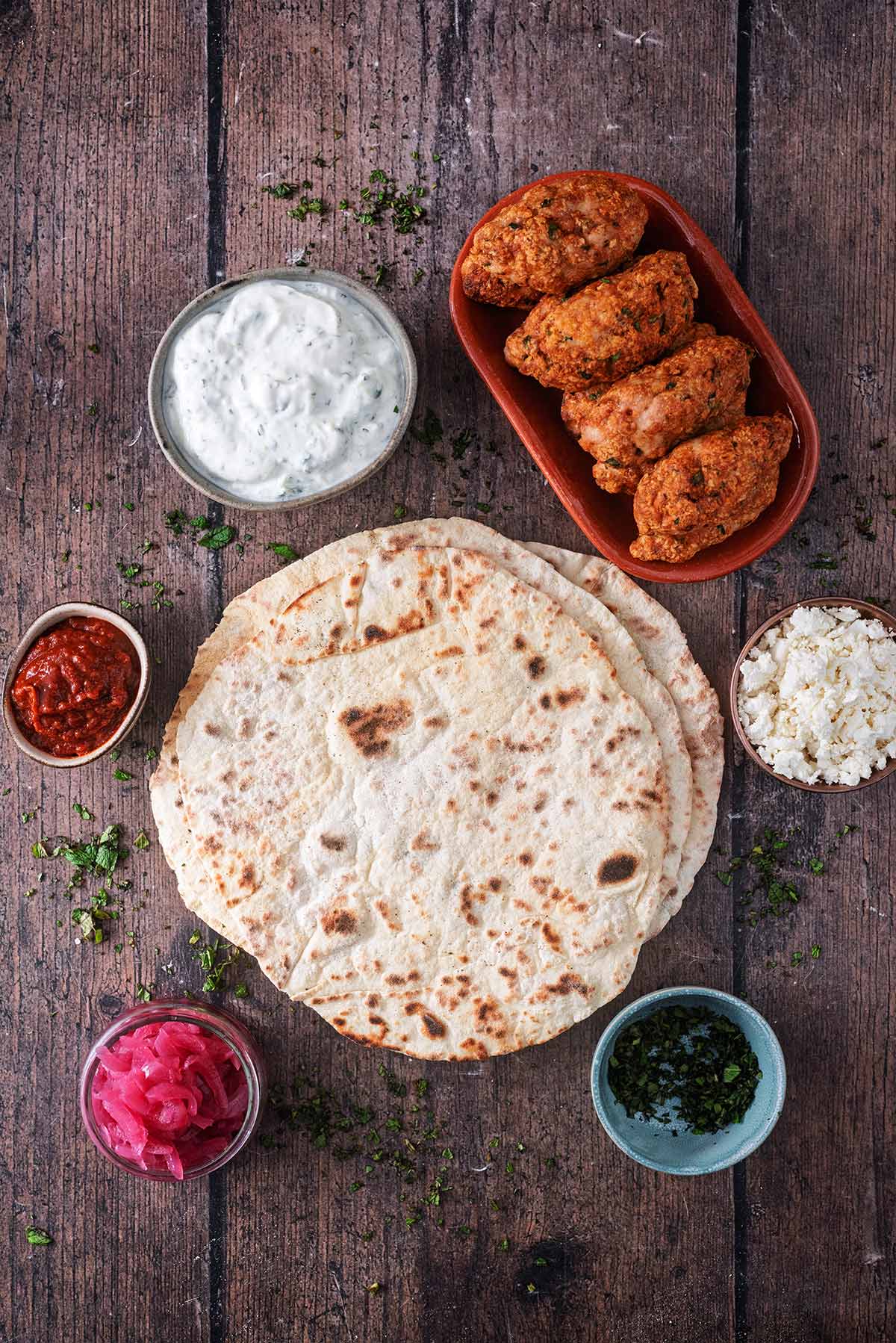 Flatbreads surrounded by koftas, sauces, feta and onions.