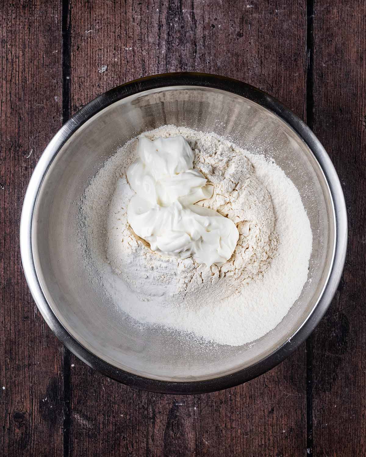 A stainless steel mixing bowl with flour and yogurt in it.