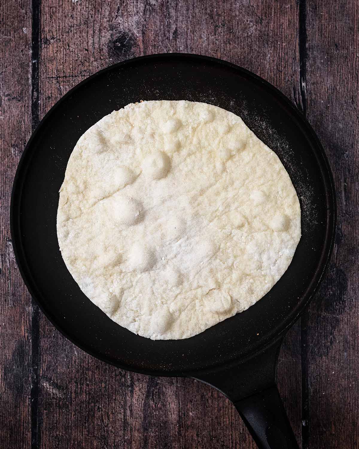 The flatbread on a flat ban with bubbles forming in the dough.