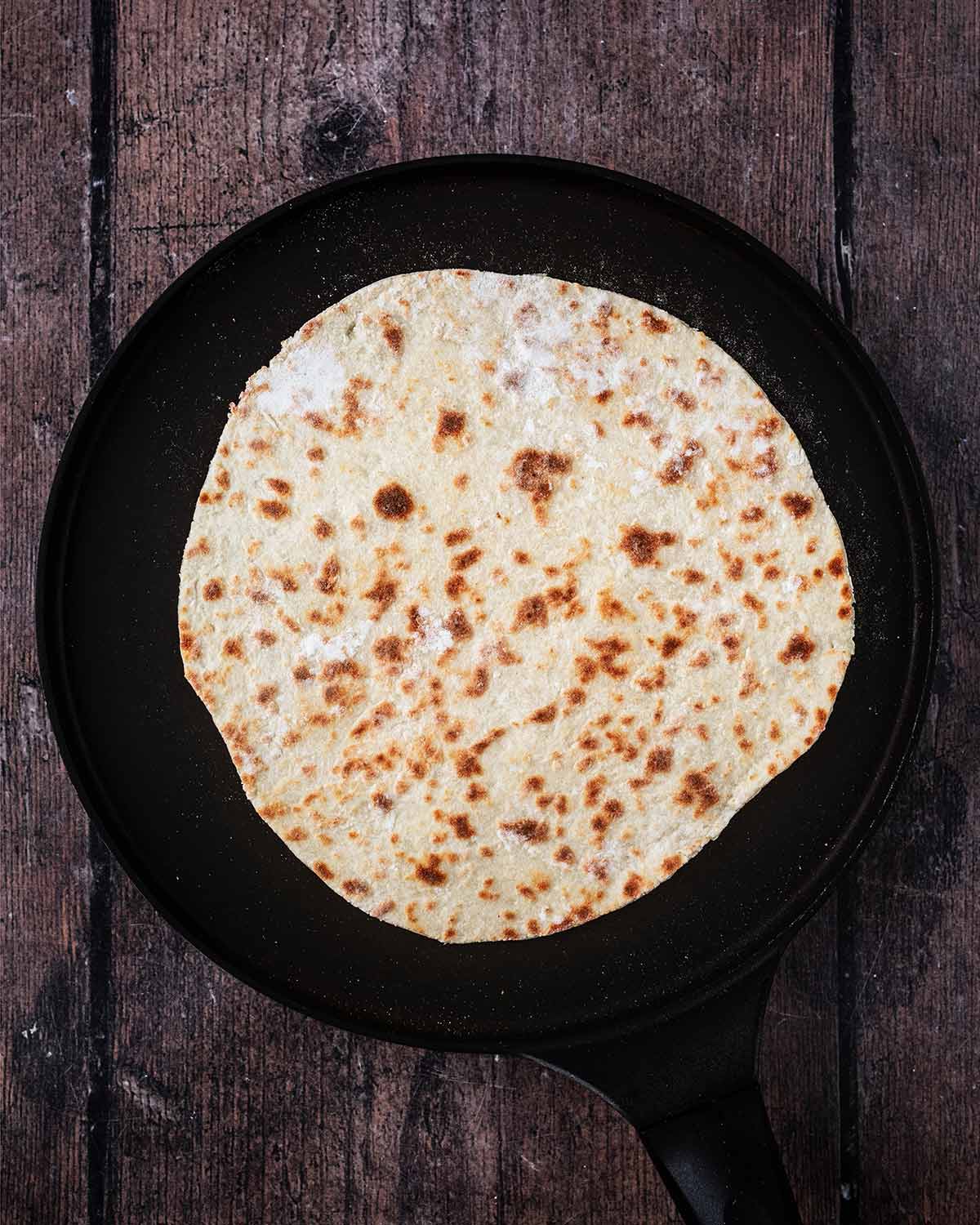 The flatbread in the pan with charred spots.