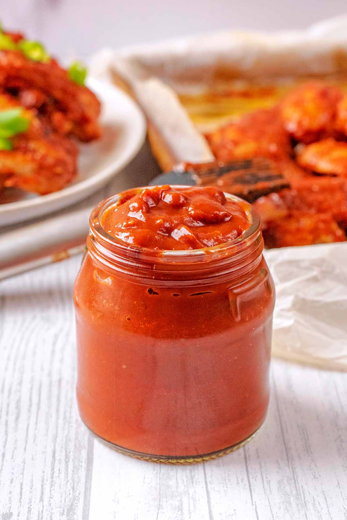 A jar of bbq sauce in front of a plate of chicken wings