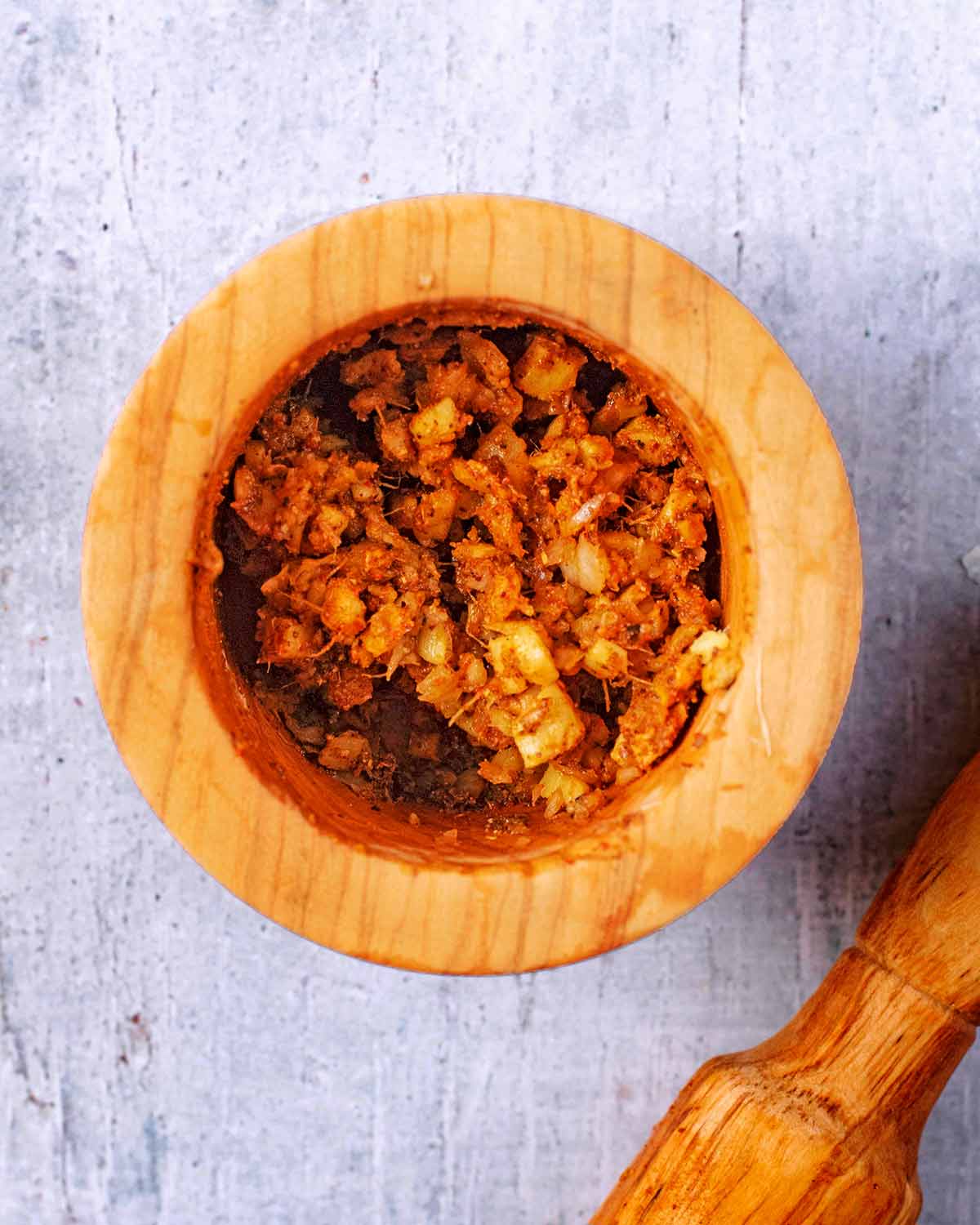A wooden pestle and mortar containing a brown curry paste.