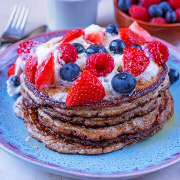 A stack of pancakes with berries and cream on top.