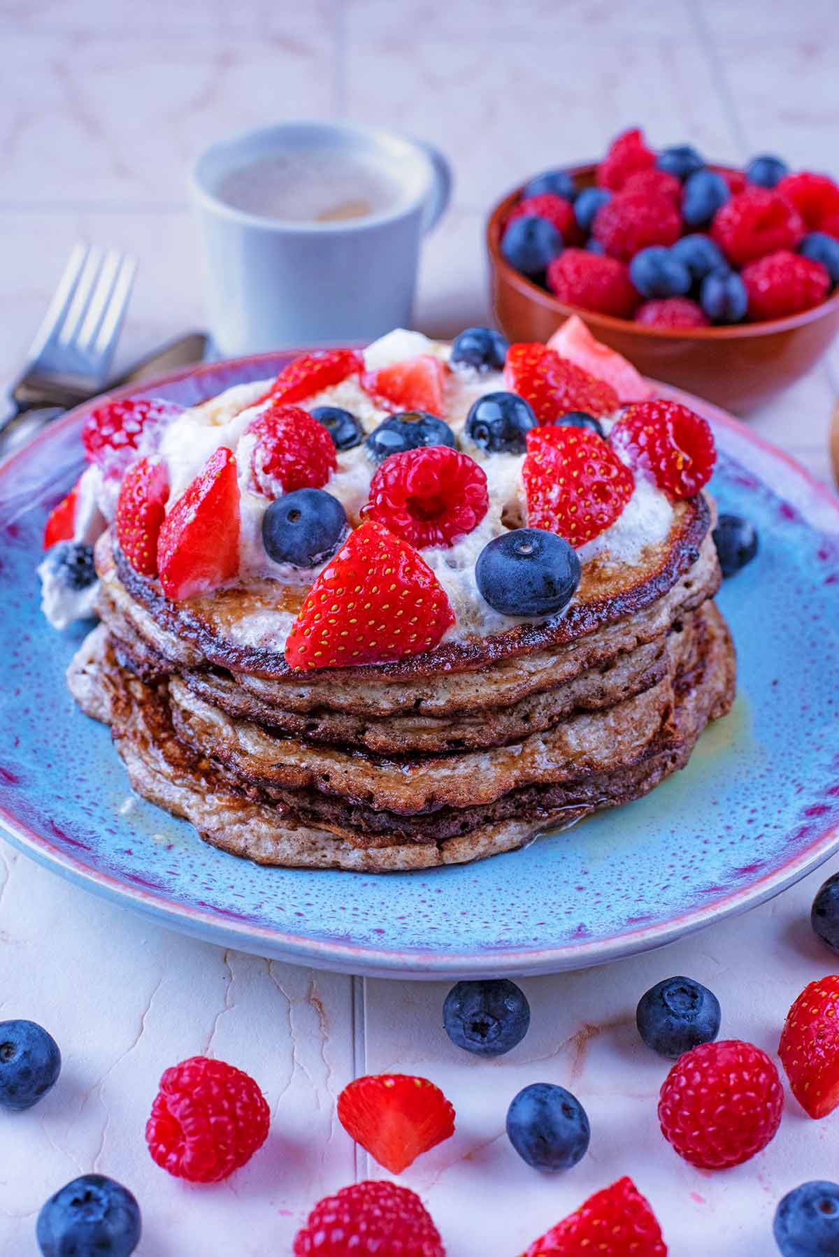A blue plate with a stack of pancakes topped with cream and berries.