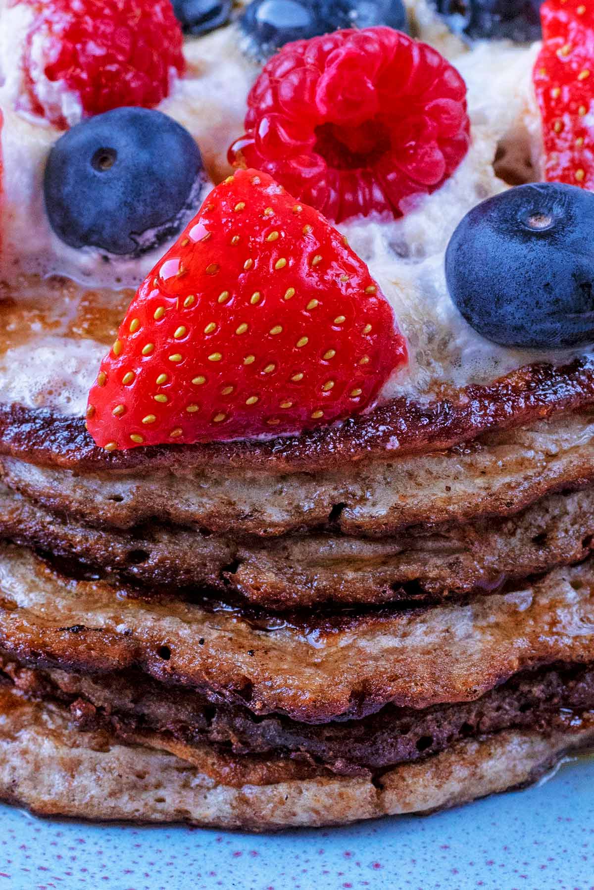 A stack of six pancakes with cream, strawberries and blueberries.