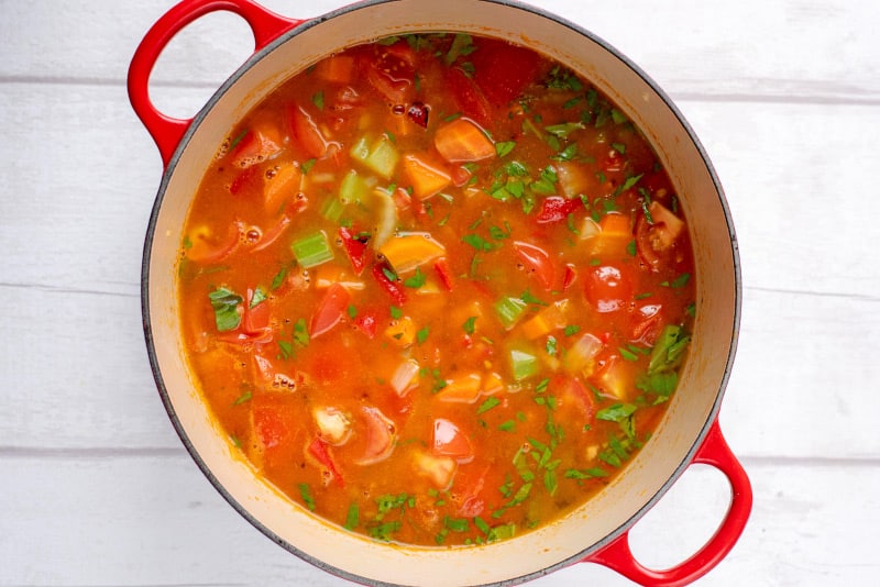 A large red pan with celery, carrots, tomatoes and stock.