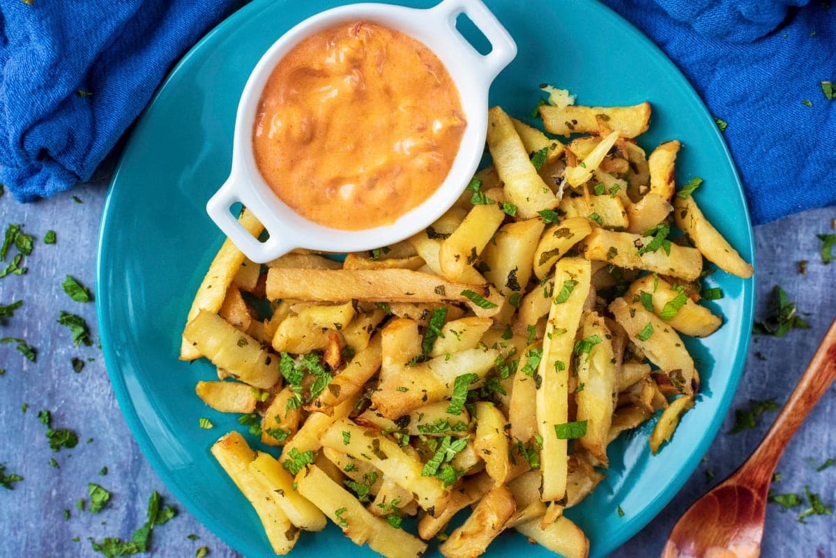 Baked Parsnip Fries on a blue plate with a small pot of chilli dip.