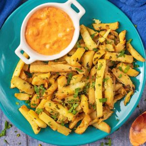 Baked Parsnip Fries on a blue plate with a small pot of chilli dip
