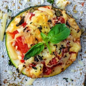 A disk of courgette covered with pizza toppings and basil leaves