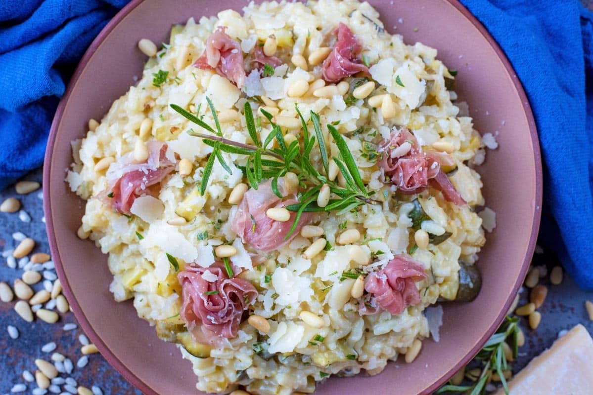 Courgette Risotto with Parma Ham in a pink bowl with rosemary sprig on top.