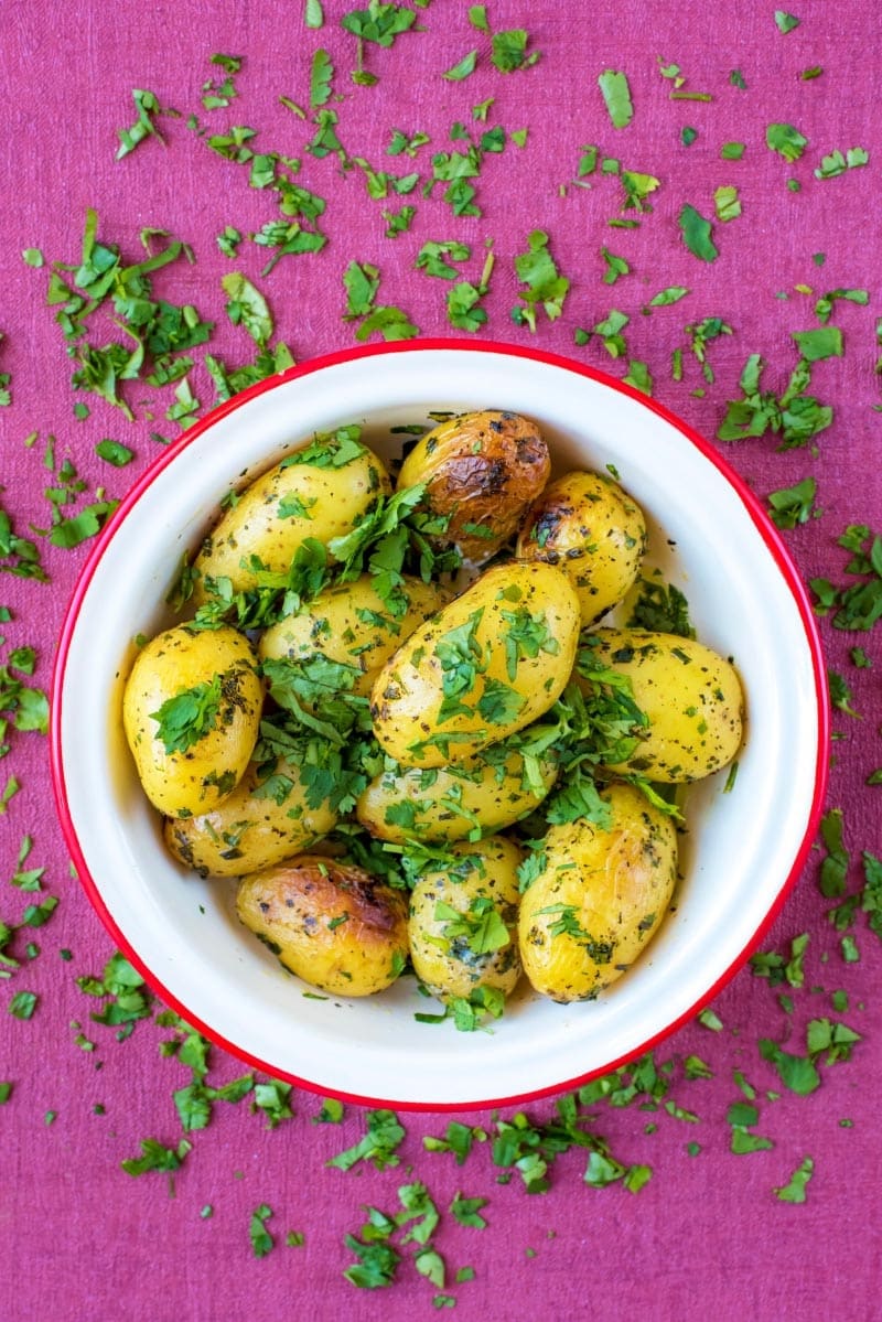 A white bowl full of roasted potatoes on a purple surface.