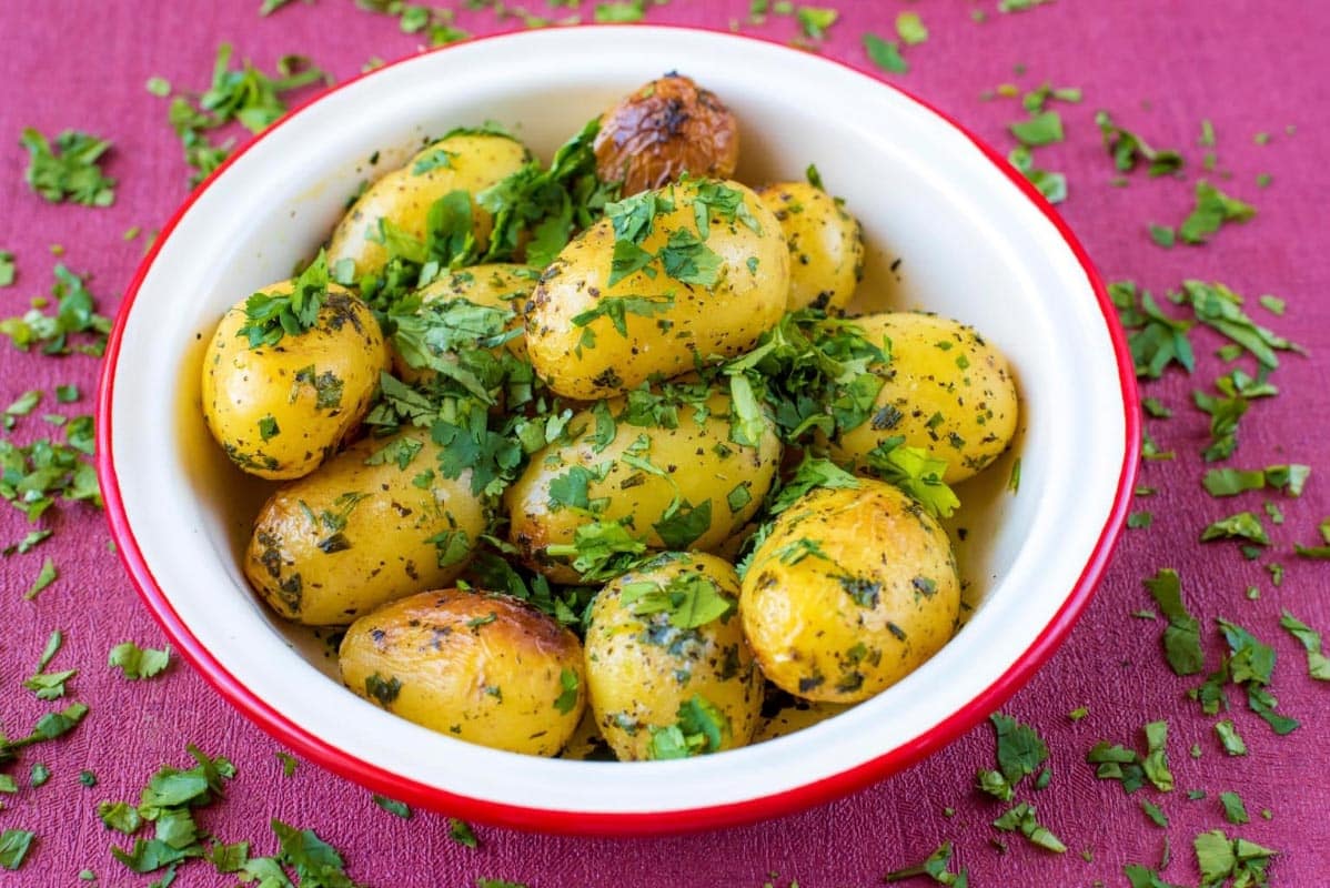 A bowl of Four Herb Roasted Potatoes in a red rimmed white bowl.