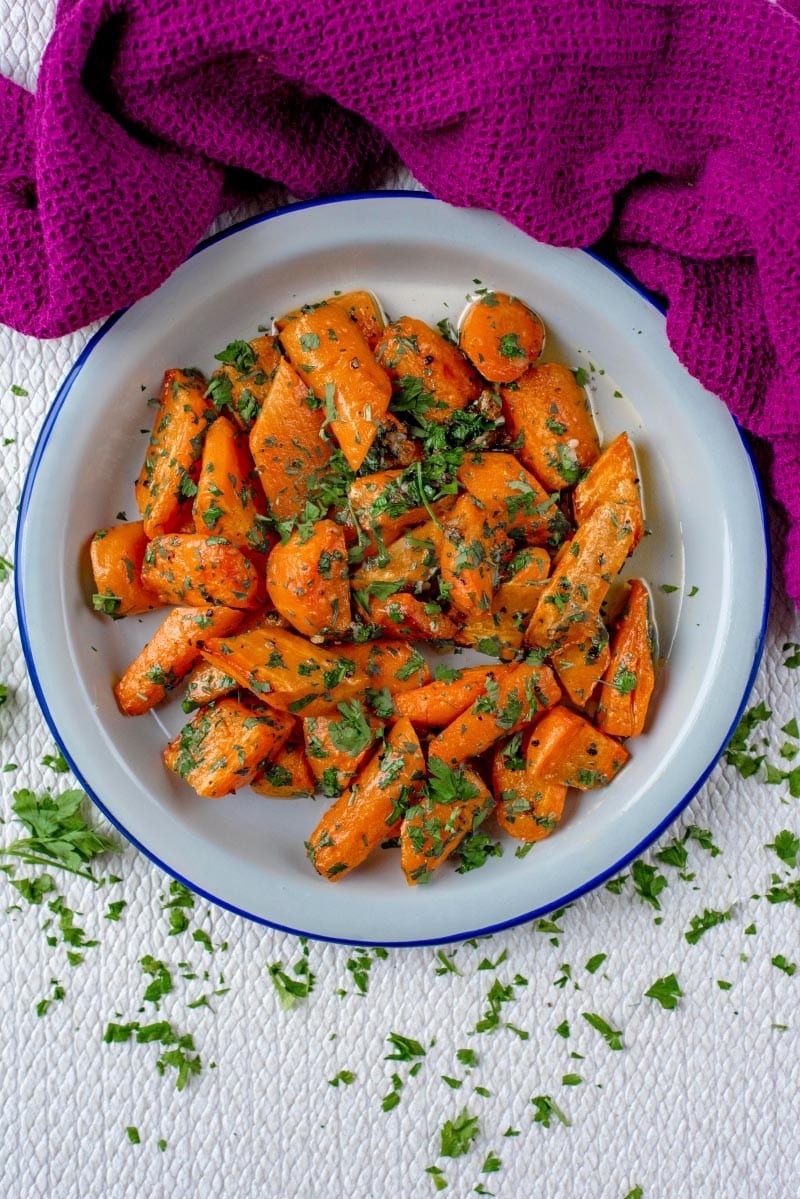 A white bowl full of roasted carrots, next to a purple towel.