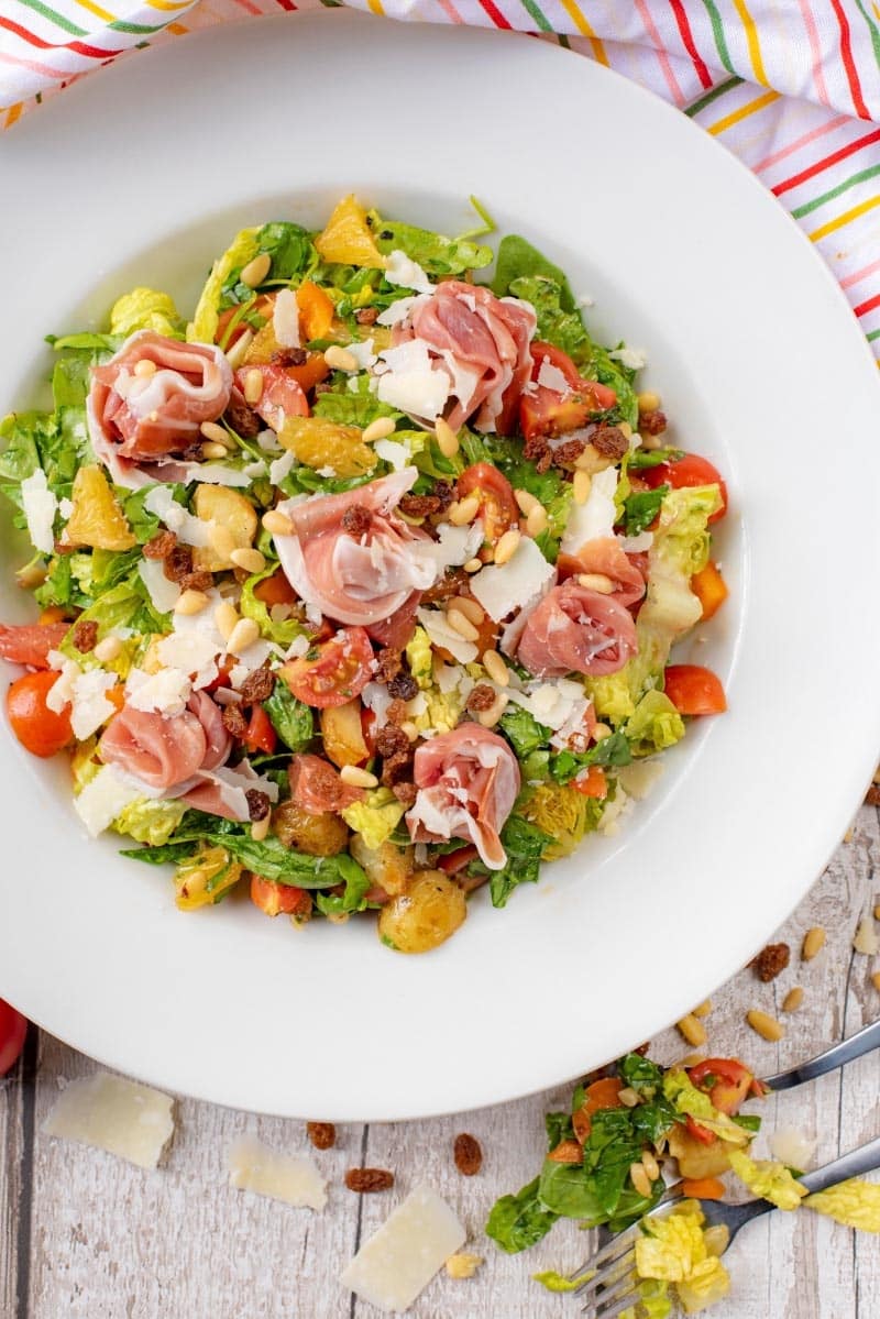 Parma ham sat upon a chopped salad containing leaves, tomatoes, fruit and nuts.